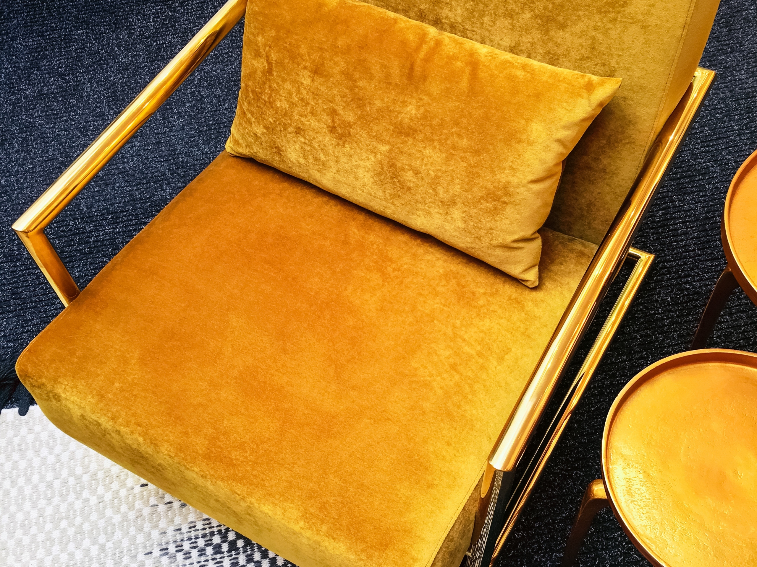 Dark yellow velvet armchair and golden side table. Modern furniture with retro feel.